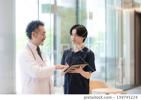 畫面中,醫生一邊看著平板電腦一邊給予指示和傳遞訊息,旁邊還有一位新來的醫生或護士,這體現了醫療領域的數位轉型(DX)和團隊合作。 畫面中,醫生一邊看著平板電腦一邊給予指示和傳遞訊息,旁邊還有一位新來的醫生或護士,這體現了醫療領域的數位轉型(DX)和團隊合作。 139745224