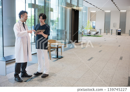 醫生看著平板電腦,一邊給予指示一邊傳遞訊息,與新來的醫生和護士團隊合作(全身像)。 醫生看著平板電腦,一邊給予指示一邊傳遞訊息,與新來的醫生和護士團隊合作(全身像)。 139745227