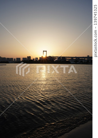 A vertical composition captures the setting sun sinking behind the main towers of the Rainbow Bridge and the sunlit road of Tokyo Bay. A vertical composition captures the setting sun sinking behind the main towers of the Rainbow Bridge and the sunlit road of Tokyo Bay. 139745325