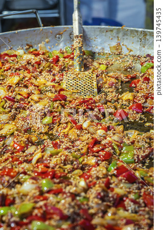 Preparing paella, Spanish rice dish with vegetables and other ingredients. Dish is cooked in large, flat pan with metal spatula. Concept of grill, street food, catering, cuisine Preparing paella, Spanish rice dish with vegetables and other ingredients. Dish is cooked in large, flat pan with metal spatula. Concept of grill, street food, catering, cuisine 139745435