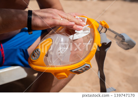 Caucasian man cleaning full face snorkeling mask on beach at Red Sea resort in Sharm El Sheikh Egypt. Travel and diving lifestyle Caucasian man cleaning full face snorkeling mask on beach at Red Sea resort in Sharm El Sheikh Egypt. Travel and diving lifestyle 139747170