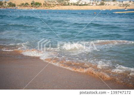 Sea waves wash sandy beach on Red Sea coast in Sharm El Sheikh Egypt with resort shoreline and sunny summer weather. Resort lifestyle and tourism Sea waves wash sandy beach on Red Sea coast in Sharm El Sheikh Egypt with resort shoreline and sunny summer weather. Resort lifestyle and tourism 139747172