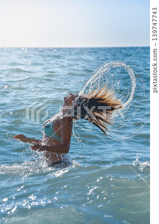 Woman flipping wet hair in sea water during sunny summer vacation Woman flipping wet hair in sea water during sunny summer vacation 139747743