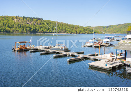 Scenic marina with boats on calm blue lake surrounded by green hills and forest under clear sunny sky in summer. Scenic marina with boats on calm blue lake surrounded by green hills and forest under clear sunny sky in summer. 139748218