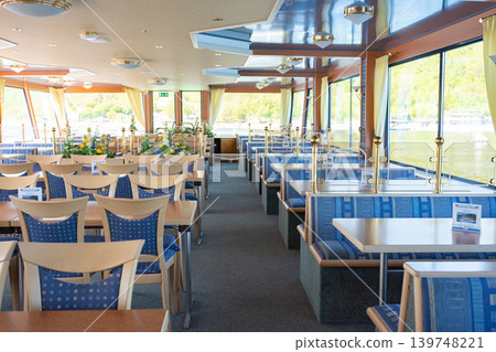 Bright restaurant interior with tables and chairs inside modern passenger cruise ship. Cozy dining area with panoramic windows and daylight. Bright restaurant interior with tables and chairs inside modern passenger cruise ship. Cozy dining area with panoramic windows and daylight. 139748221