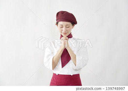 Female pastry chef/baker/cafe employee praying against a white background. Female pastry chef/baker/cafe employee praying against a white background. 139748997