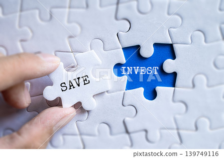 Hand fitting Save and Invest blue puzzle pieces together on gray jigsaw background, personal finance and wealth management concept 139749116