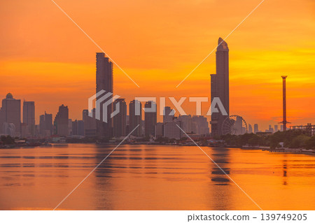 Vibrant orange sunset over a sprawling city skyline reflected in a calm river Vibrant orange sunset over a sprawling city skyline reflected in a calm river 139749205
