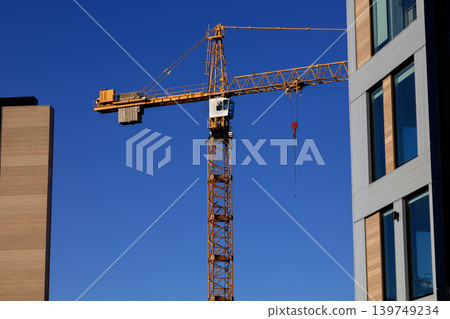 Tower crane between modern buildings against clear blue sky, urban construction Tower crane between modern buildings against clear blue sky, urban construction 139749234