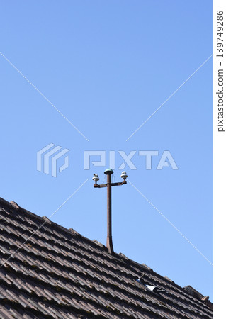 Old utility pole on a tiled house roof under blue sky 139749286