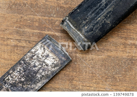 Close-Up of a Broken Iron Sickle Detached from Its Handle, Showing Clear Fracture Point on a Rustic Aged Wooden Surface Background Close-Up of a Broken Iron Sickle Detached from Its Handle, Showing Clear Fracture Point on a Rustic Aged Wooden Surface Background 139749878