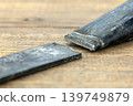 Close-Up of a Broken Iron Sickle Blade Separated from Its Handle on a Rustic Wooden Surface, Showing a Clear and Detailed Metal Fracture Break Point in Sharp Focus 139749879