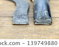 Two Pieces of a Broken Iron Sickle Lying on Wooden Surface Showing a Clear Fracture Break Point Where the Blade Separated From Its Handle Due to Damage 139749880