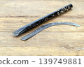 Old Broken Iron Sickle with Curved Blade Separated from Its Worn Black Handle on a Rustic Wooden Background Showing Clear Break Point and Aged Metal Texture 139749881