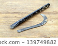 Old Worn Broken Iron Sickle Blade Separated from Its Black Handle Lying on a Rustic Wooden Surface, Showing Clear Break Point and Heavy Use 139749882