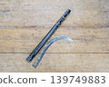 Old Worn Broken Iron Sickle Blade Separated From Its Black Metal Handle Lying Flat on a Rustic Weathered Wooden Plank Surface Showing Clear Break Point 139749883