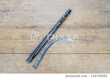 Old Worn Broken Iron Sickle Blade Separated From Its Black Metal Handle Lying Flat on a Rustic Weathered Wooden Plank Surface Showing Clear Break Point Old Worn Broken Iron Sickle Blade Separated From Its Black Metal Handle Lying Flat on a Rustic Weathered Wooden Plank Surface Showing Clear Break Point 139749883