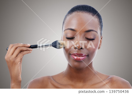 Brush, makeup and black woman, face and beauty with foundation for cosmetics and wellness isolated on grey background. Shine, cosmetology and tools to apply powder, skin glow and shimmer in studio 139750436