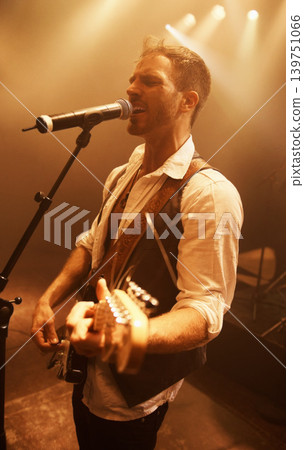 Singer, music and guitar with man on stage for concert, performance and rock show. Event, spotlight and energy with male musician playing instrument at festival club for rave, disco and celebration Singer, music and guitar with man on stage for concert, performance and rock show. Event, spotlight and energy with male musician playing instrument at festival club for rave, disco and celebration 139751066