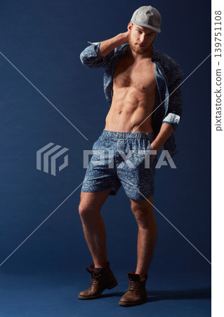 Fashion, portrait or model with six pack in studio on a blue background in an open unbuttoned shirt. Body, chest or handsome male person posing on color wall for masculine style with a trendy cap Fashion, portrait or model with six pack in studio on a blue background in an open unbuttoned shirt. Body, chest or handsome male person posing on color wall for masculine style with a trendy cap 139751108