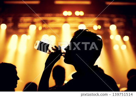 Night, club and man with a drink at party, event or music festival with stage lights and silhouette. Dark, concert and person dance with bottle of alcohol in crowd at social celebration or rave Night, club and man with a drink at party, event or music festival with stage lights and silhouette. Dark, concert and person dance with bottle of alcohol in crowd at social celebration or rave 139751514