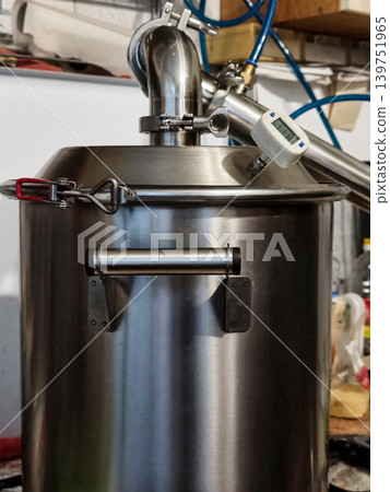 A brewing kettle with a silver finish and a digital temperature gauge sits in a brewing area filled with tools and equipment 139751965
