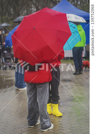 People standing under bright umbrellas during rain in public park, wet pavement, colorful rainwear, blurred background. Concept of umbrella protection, weather, season, event 139752068