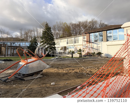 an orange-handled metal wheelbarrow lies tipped on its side on the rough, dirt-covered ground. Outdoor construction or renovation site an orange-handled metal wheelbarrow lies tipped on its side on the rough, dirt-covered ground. Outdoor construction or renovation site 139752110