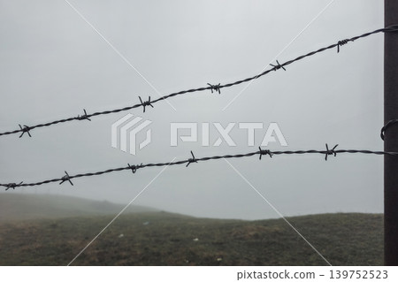 Damp fog blankets the hillside behind barbed wire 139752523