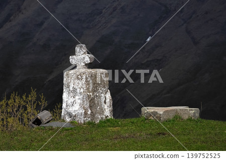 Weathered stone cross stands alone on grassy hillside 139752525