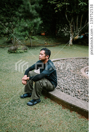 Southeast Asian Man Sitting Thoughtfully on Grass Outdoors 139752538