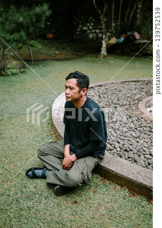 Thoughtful Southeast Asian Male Sitting on Grass in Nature 139752539