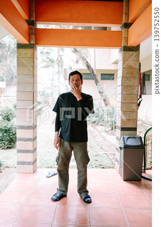 Southeast Asian Man Standing While Smoking in Semi Outdoor Area Southeast Asian Man Standing While Smoking in Semi Outdoor Area 139752550
