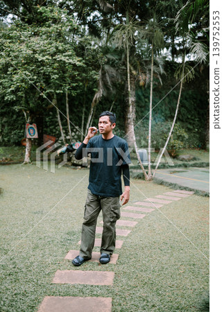 Asian Male Standing and Smoking in Outdoor Park Area Asian Male Standing and Smoking in Outdoor Park Area 139752553