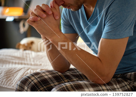 Stressed man sitting on bed with clasped hands at home Stressed man sitting on bed with clasped hands at home 139752827