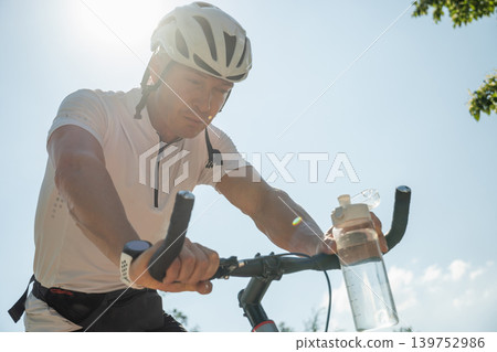 Male cyclist sitting on bike and drinking water Male cyclist sitting on bike and drinking water 139752986