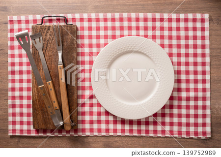 BBQ tools and white plate minimal table setting on checkered cloth top view BBQ tools and white plate minimal table setting on checkered cloth top view 139752989