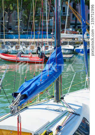 Detailed view of sailboat mast, ropes and blue sail cover, showcasing nautical equipment, sailing lifestyle and technical rigging elements Detailed view of sailboat mast, ropes and blue sail cover, showcasing nautical equipment, sailing lifestyle and technical rigging elements 139752996