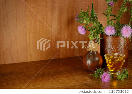 Natural herbal oil from thistle seeds with blooming wild flowers and rustic pottery on vintage wood surface 139753012