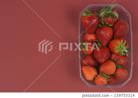 Fresh strawberries in plastic punnet on red background Fresh strawberries in plastic punnet on red background 139753314