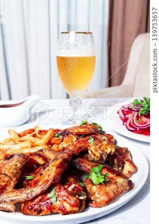 Delicious barbecue chicken wings, with French fries, salad and a refreshing drink, at a cozy table, there are no people Delicious barbecue chicken wings, with French fries, salad and a refreshing drink, at a cozy table, there are no people 139753657