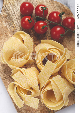 raw pappardelle pasta, on a wooden chopping board, with cherry tomatoes, top view, no people, raw pappardelle pasta, on a wooden chopping board, with cherry tomatoes, top view, no people, 139753658