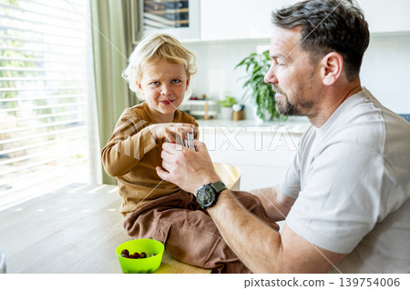 Dad feeding toddler during family mealtime in modern kitchen. Dad feeding toddler during family mealtime in modern kitchen. 139754006