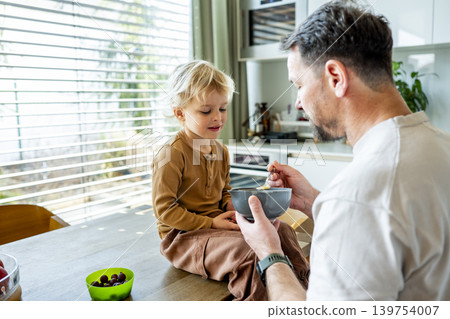Dad feeding toddler during family mealtime in modern kitchen. Dad feeding toddler during family mealtime in modern kitchen. 139754007