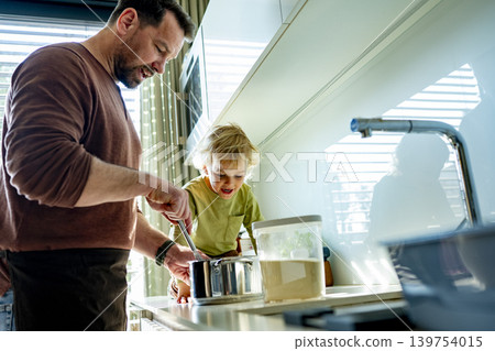 Dad and toddler preparing simple meal together in bright kitchen. Dad and toddler preparing simple meal together in bright kitchen. 139754015