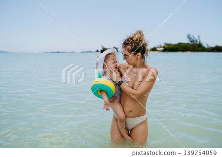 Mother holding cying daughter, standin in sea water. Mother holding cying daughter, standin in sea water. 139754059