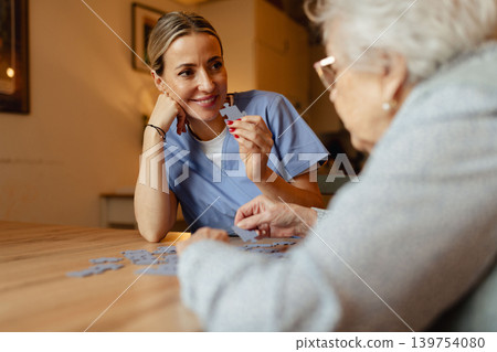 Friendly caregiver and elderly patient working on puzzle together, having fun. Friendly caregiver and elderly patient working on puzzle together, having fun. 139754080