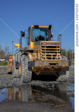Yellow wheel loader front end on muddy construction site against blue sky Yellow wheel loader front end on muddy construction site against blue sky 139754145