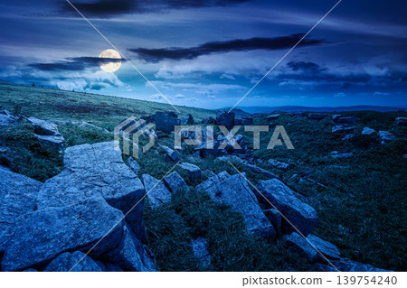 mountainous landscape during summertime at night. full moon over boulders and rock formations surrounded grassy hills. picture of an untouched highland. backdrop for fiction art or mystery concept mountainous landscape during summertime at night. full moon over boulders and rock formations surrounded grassy hills. picture of an untouched highland. backdrop for fiction art or mystery concept 139754240