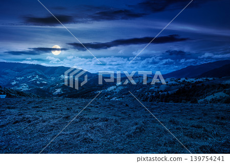 mountain landscape with grassy field at night. full moon over trees on the rolling hills and rural valley beneath a dark sky in the background. mysterious view of carpathian mountains in summer mountain landscape with grassy field at night. full moon over trees on the rolling hills and rural valley beneath a dark sky in the background. mysterious view of carpathian mountains in summer 139754241